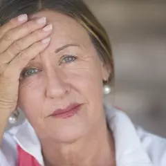 Zmęczona kobieta z ręką na czole, być może rozważa hormonalną terapię zastępczą.