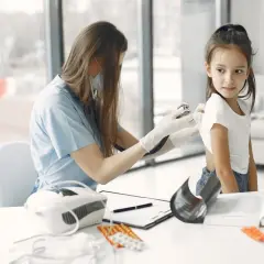 Lekarka bada dziecko stetoskopem, sprawdzając, czy nie ma guza Wilmsa. Na stole leki i inhalator.