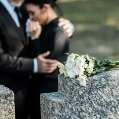 Para wspiera się na cmentarzu, obok wiązanki białych kwiatów. Czas na urlop macierzyński po poronieniu, by przeżyć żałobę.