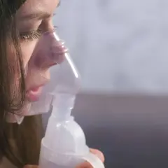 Dziewczynka z maską inhalatora na twarzy, która pomaga jej w walce z anoro.