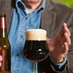Mężczyzna trzyma butelkę piwa obok pełnego kufla. Czy po szczepieniu można pić alkohol? To pytanie nurtuje wielu.