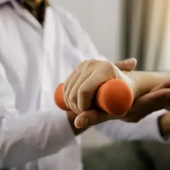 Fizjoterapeuta pomaga pacjentowi ćwiczyć rękę z hantlem, by zapobiec zanikowi mięśni.