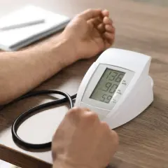 Pomiar ciśnienia przy zawale. Wynik 136/90 mmHg, puls 59. Obok szklanka wody i notatnik.