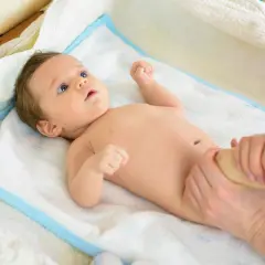 Niemowlę na ręczniku, któremu masowane są nóżki. Dbanie o rozwój dziecka, by uniknąć krzywicy.