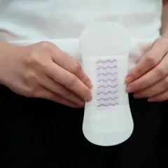 Dłonie trzymają wkładkę higieniczną. Czy to krwawienie implantacyjne a okres?