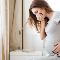 Kobieta w ciąży czuje mdłości, zasłania usta dłonią. To częste wymioty w ciąży.