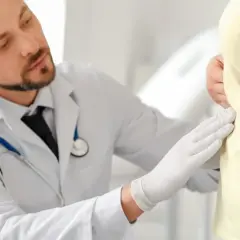 Lekarz w białym kitlu i rękawiczkach bada pacjenta. Może to być badanie profilaktyczne, np. przed zastosowaniem leku Ursopol 300.