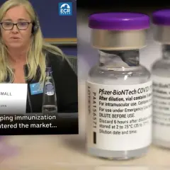Dwie fiolki szczepionki Pfizer-BioNTech COVID-19 obok kobiety przemawiającej na tle flagi UE.