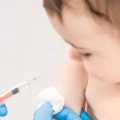 Ręka w niebieskiej rękawiczce przygotowuje do podania szczepionki Synflorix dziecku.