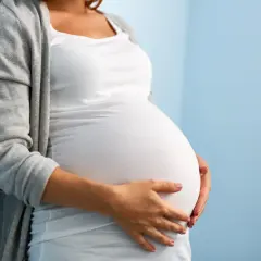 Po walce z rakiem trzonu macicy, teraz czeka na dziecko. Brzuch ciężarnej kobiety w białej bluzce i szarym kardiganie.