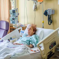 Starsza kobieta w szpitalnym łóżku z sondą. Czy opiekun medyczny może karmić przez sondę? Pielęgniarka monitoruje jej stan.