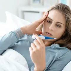 Kobieta w łóżku z termometrem, martwi się o zdrowie, obawiając się listeriozy.