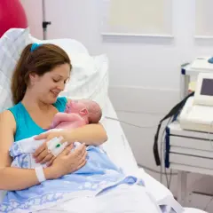 Szczęśliwa mama tuli noworodka po cesarce francuskiej. W tle sprzęt medyczny.