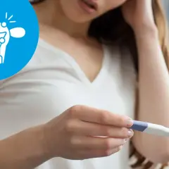 Kobieta trzyma test ciążowy, a obok widnieje symbol probella z zaznaczonymi problemami z płodnością.