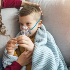 Chłopiec z maseczką nebulizatora, otulony kocem, czuje się jakby dopadła go klątwa Ondyny. Mama czule go głaszcze.