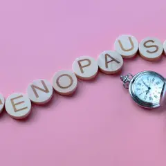 Drewniane kółka z literami układają napis "MENOPAUSE" obok kieszonkowego zegarka. Pytanie "ile trwa menopauza forum" nasuwa się samo.