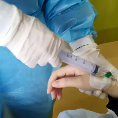Ręka pacjenta z wenflonem, pielęgniarka w rękawiczkach podaje lek, prawdopodobnie hydroxycarbamid.