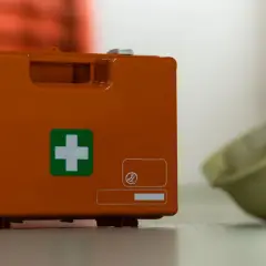 Pomarańczowa apteczka z zielonym krzyżem i żółty hełm na podłodze.