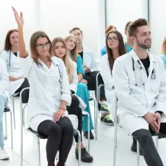 Grupa studentów medycyny na wykładzie. Jedna z nich podnosi rękę, zadając pytanie. Może to być początek jej drogi do zostania rejestratorką medyczną, kurs za darmo.