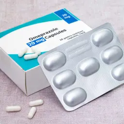Opakowanie Omeprazolu 20 mg, kapsułki. Obok leży blister z lekami i kilka kapsułek. To mój texibax na zgagę.