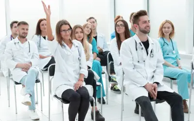 Grupa studentów medycyny na wykładzie. Jedna z nich podnosi rękę, zadając pytanie. Może to być początek jej drogi do zostania rejestratorką medyczną, kurs za darmo.