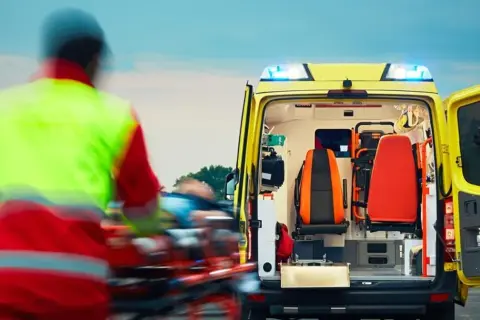 Ratownik medyczny w kamizelce odblaskowej transportuje pacjenta do karetki.