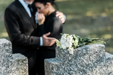 Para wspiera się na cmentarzu, obok wiązanki białych kwiatów. Czas na urlop macierzyński po poronieniu, by przeżyć żałobę.