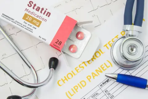 Lekarz bada wyniki cholesterolu, obok leży stetoskop i opakowanie leku Statin 20 mg.