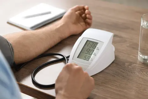 Pomiar ciśnienia przy zawale. Wynik 136/90 mmHg, puls 59. Obok szklanka wody i notatnik.
