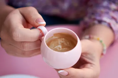 Delikatna kawa w różowej filiżance, trzymana w dłoniach z francuskim manicure. Chwila relaksu, nawet w ciąży.