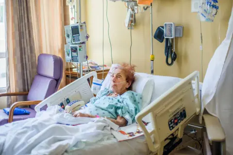 Starsza kobieta w szpitalnym łóżku z sondą. Czy opiekun medyczny może karmić przez sondę? Pielęgniarka monitoruje jej stan.