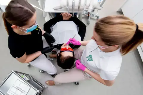 Dwie asystentki stomatologiczne pracują przy pacjencie. Zastanawiasz się, ile zarabia asystentka stomatologiczna?