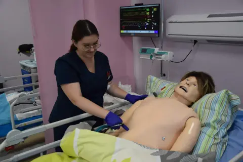Studentka medycyny ćwiczy procedury medyczne na fantomie. Monitor pokazuje parametry życiowe.