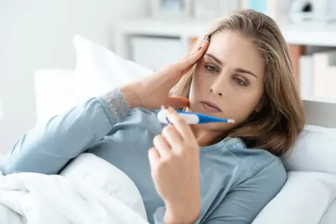 Kobieta w łóżku z termometrem, martwi się o zdrowie, obawiając się listeriozy.