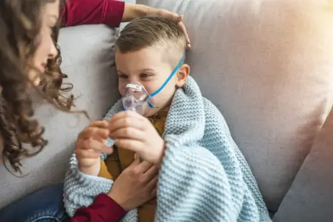 Chłopiec z maseczką nebulizatora, otulony kocem, czuje się jakby dopadła go klątwa Ondyny. Mama czule go głaszcze.