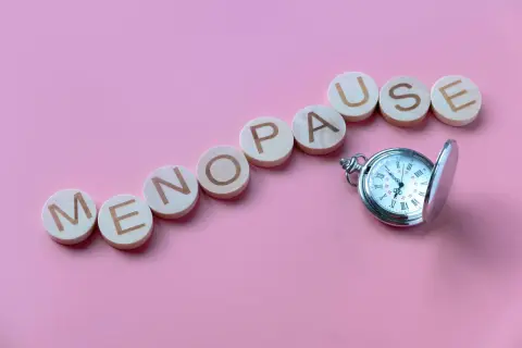 Drewniane kółka z literami układają napis "MENOPAUSE" obok kieszonkowego zegarka. Pytanie "ile trwa menopauza forum" nasuwa się samo.