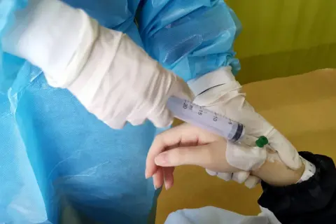 Ręka pacjenta z wenflonem, pielęgniarka w rękawiczkach podaje lek, prawdopodobnie hydroxycarbamid.