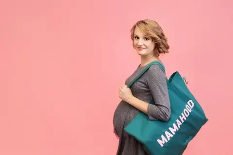Przyszła mama z torbą "Mamahood" gotowa do szpitala. Sprawdź, co zabrać do szpitala, by niczego nie zapomnieć.