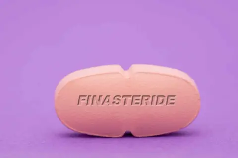 Różowa tabletka z napisem FINASTERIDE na fioletowym tle.