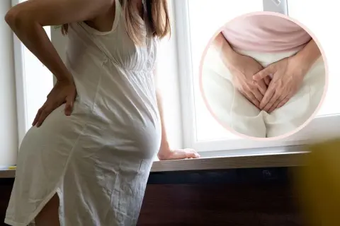 Ciężarna kobieta z dłońmi na biodrze, w okręgu zbliżenie na dłonie zakrywające krocze, sugerujące żylaki sromu w ciąży.