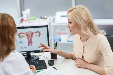 Lekarka omawia z pacjentką budowę macicy i potencjalne problemy, takie jak atonia macicy, wskazując na ekranie.