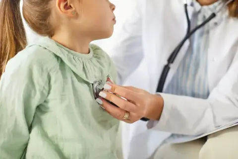 Lekarz podczas wizyty pediatrii osłuchuje małą pacjentkę stetoskopem.