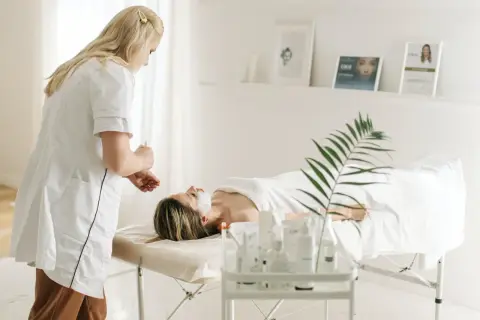 Dermatolog wykonuje zabieg na twarzy pacjentki leżącej na kozetce w gabinecie.