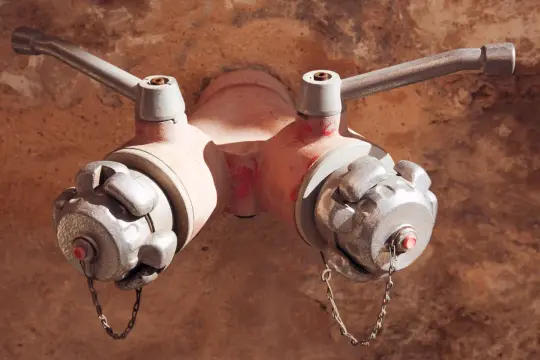 Czerwony hydrant podziemny z dwoma metalowymi uchwytami i srebrnymi zaślepkami, gotowy do akcji.