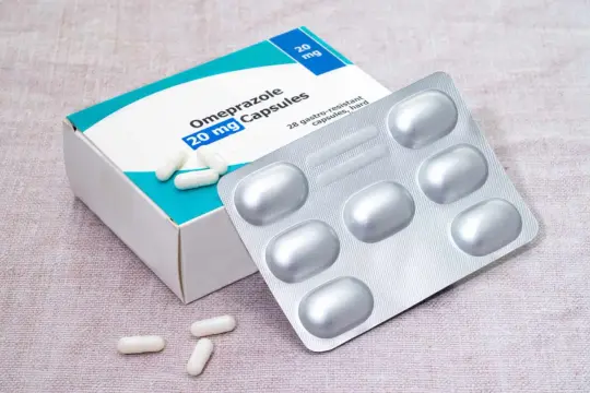 Opakowanie Omeprazolu 20 mg, kapsułki. Obok leży blister z lekami i kilka kapsułek. To mój texibax na zgagę.