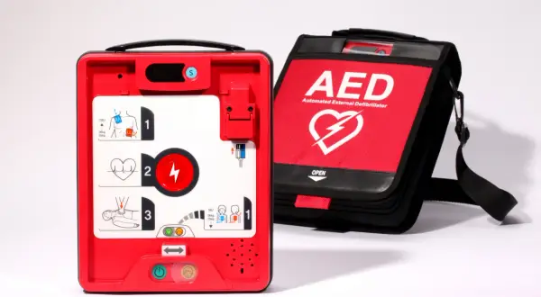 Czerwony defibrylator AED i jego czarna torba transportowa na białym tle.