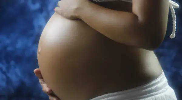 Brzuch ciężarnej kobiety, delikatnie dotykany dłońmi. Warto pamiętać o konsultacji z lekarzem w sprawie stosowania leków, np. ibuprom w ciąży.