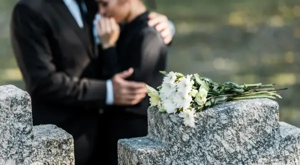 Para wspiera się na cmentarzu, obok wiązanki białych kwiatów. Czas na urlop macierzyński po poronieniu, by przeżyć żałobę.