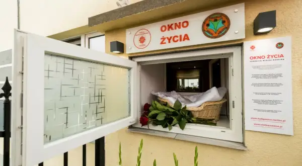 Okno życia z koszykiem, białym kocykiem i czerwonymi różami. To miejsce nadziei dla noworodków.