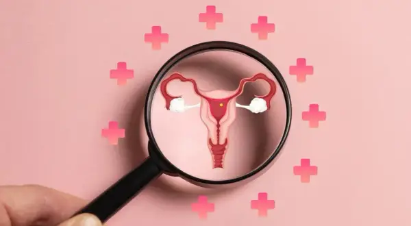 PCOS co to? Ilustracja narządów rodnych pod lupą, otoczona różowymi krzyżykami symbolizującymi zdrowie.
